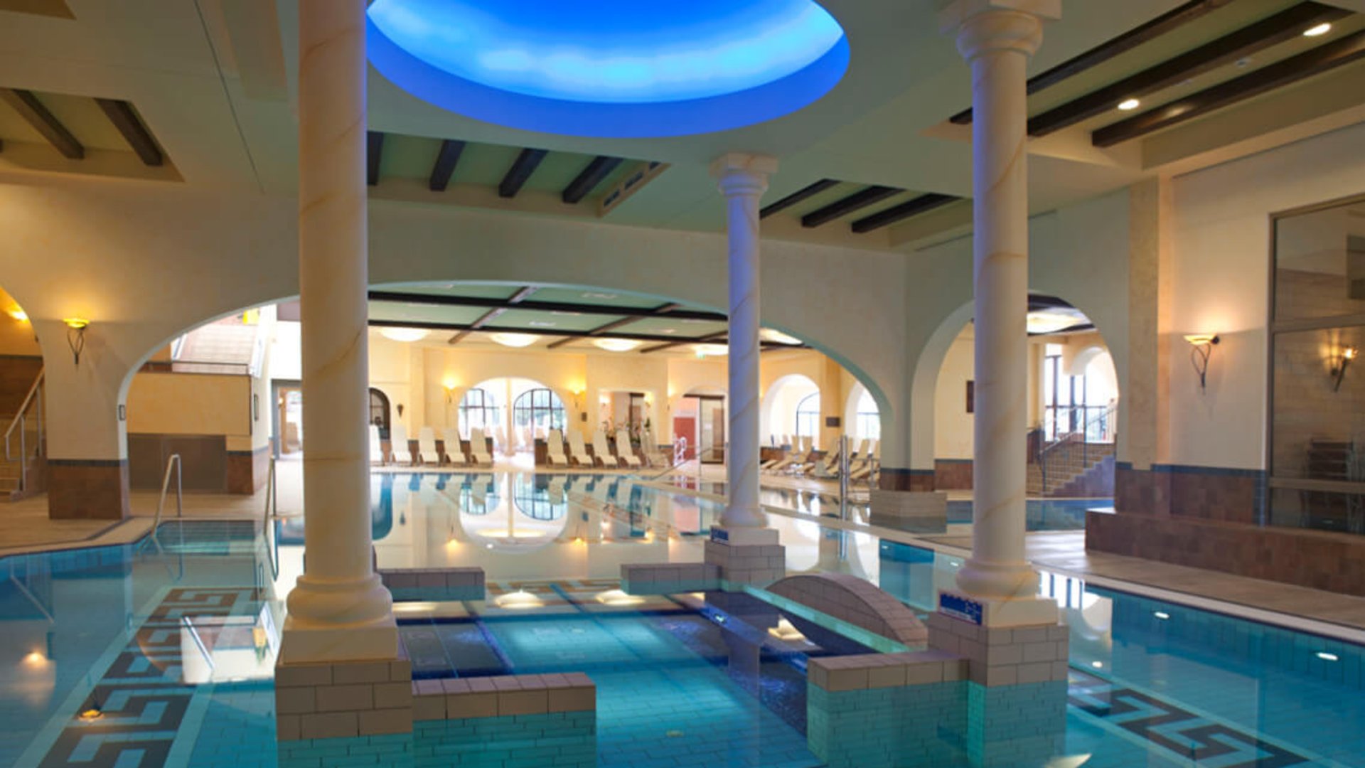 Foto: EurothermenResorts Bad Hall/Weissenbrunner: Therme Mediterrana Thermenbecken innen mit 4 Säulen und blauer Beleuchtung von oben